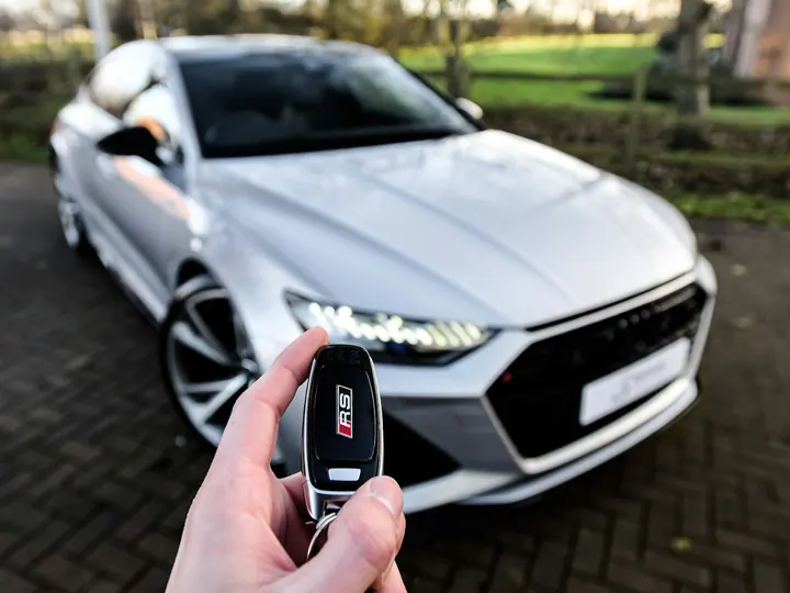 A hand holding a car key in front of a silver car