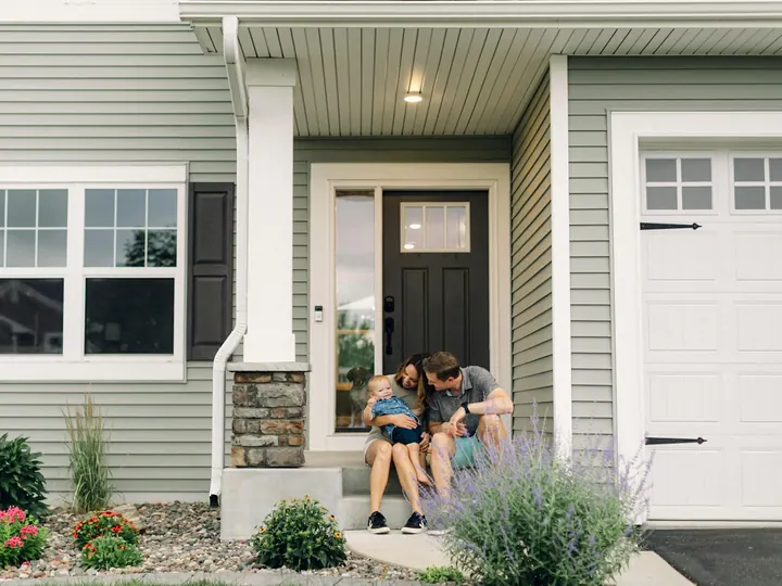 A young family sitting on the front steps of their house